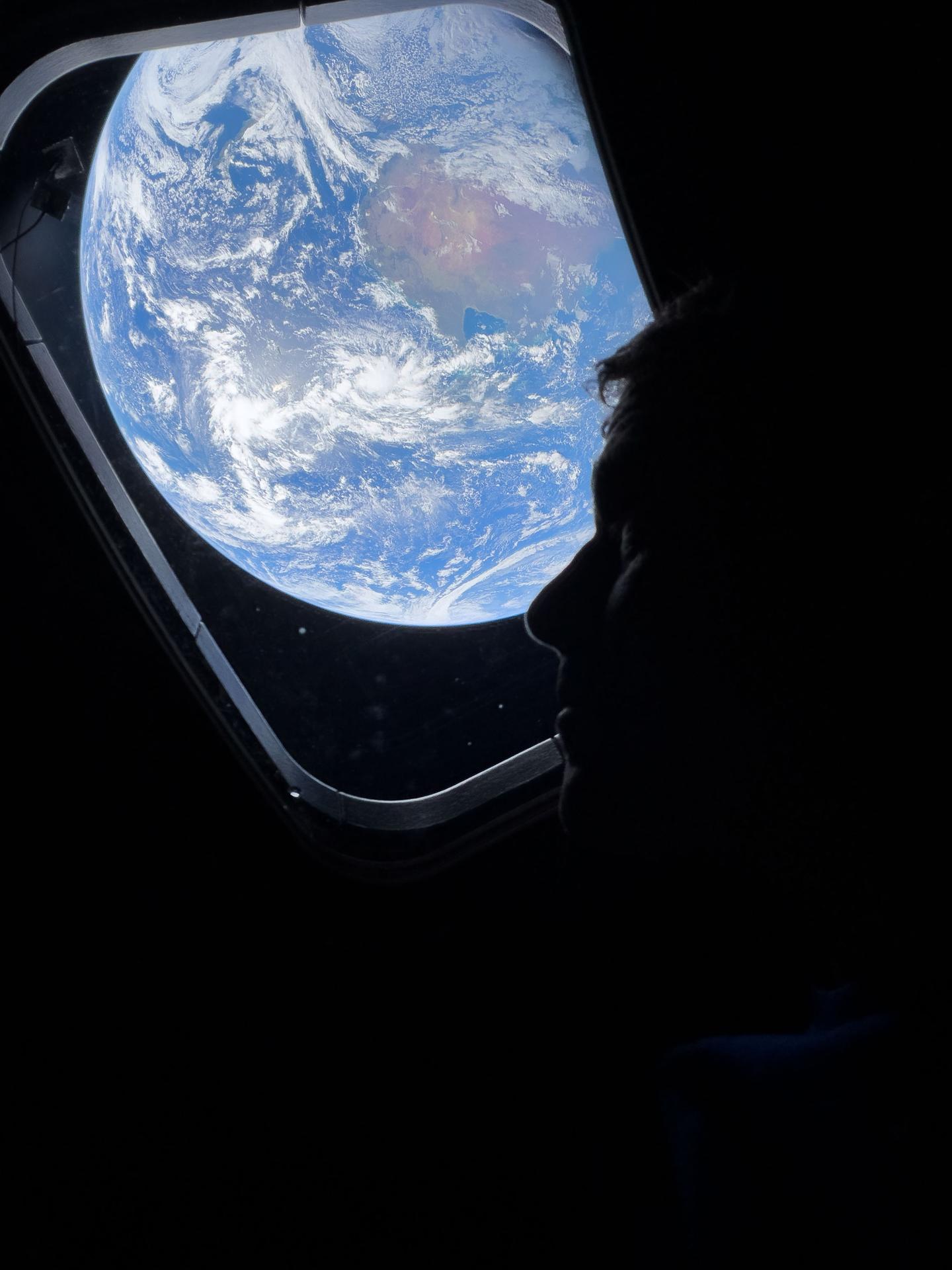 NASA astronaut and Artemis II Commander Reid Wiseman peers out of one of the Orion spacecraft's main cabin windows, looking back at Earth, as the crew travels towards the Moon.